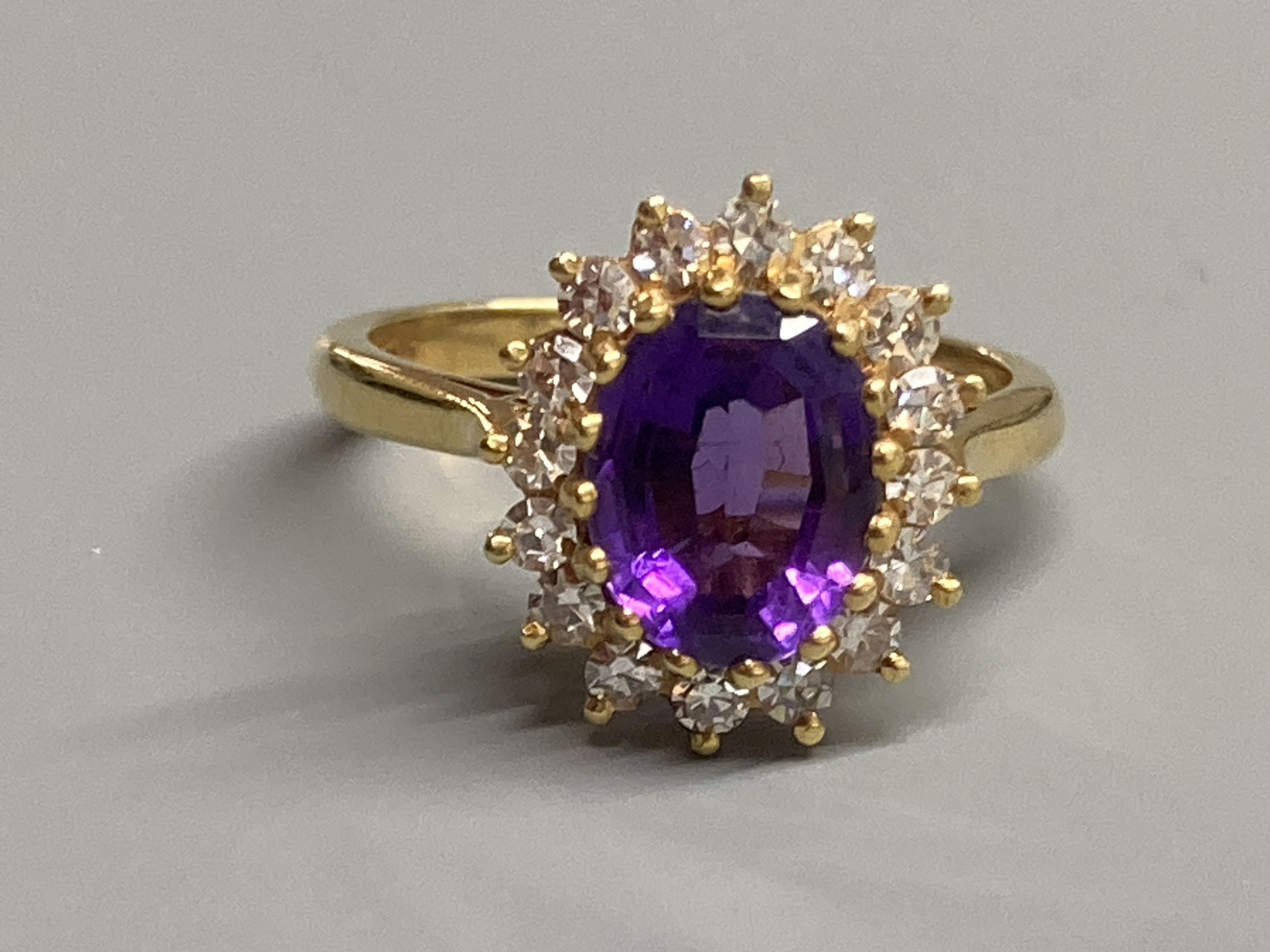 A modern 18ct gold, amethyst and diamond set oval cluster ring, size N, gross 4.9 grams.